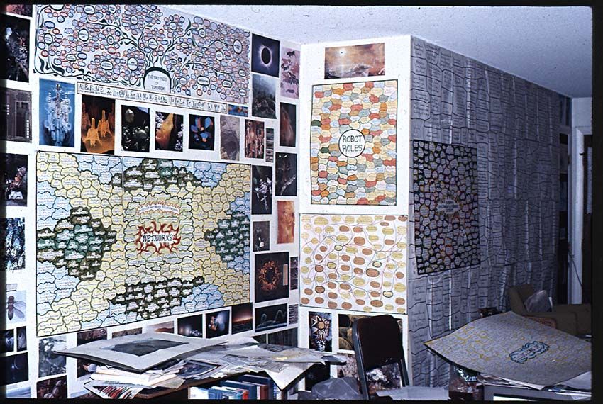 A cluttered apartment with charts on the wall